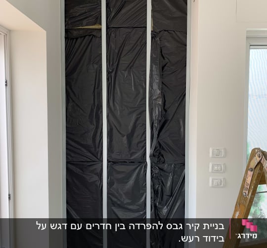 קיר גבס עם יריעות פלסטיק שחורות ומסגרת מתכת